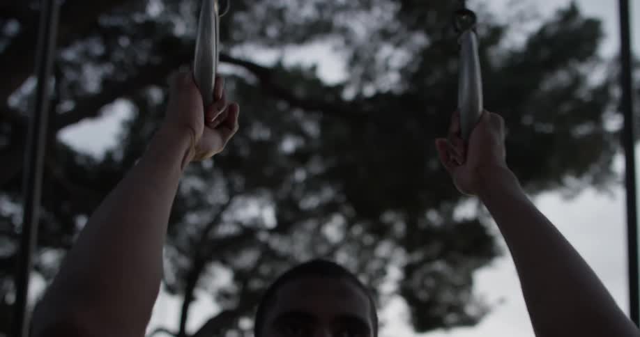 A man does pull ups with hanging rings outside