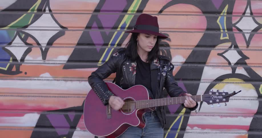 A woman stands next to a wall of playing guitar