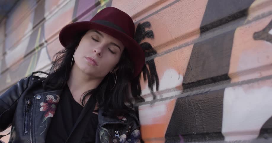 Woman in hat poses and leans against a painted wall