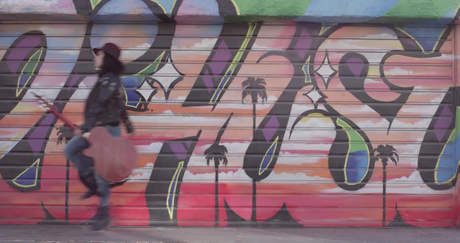 A woman skipping and carrying a guitar down a sidewalk