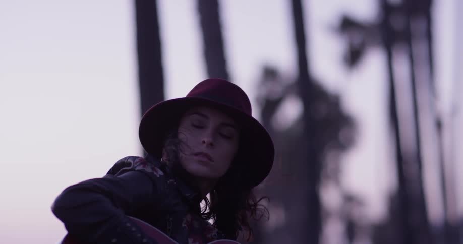 A woman in a hat on a cold day plays guitar in the park