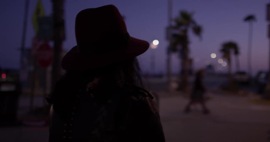 Woman wearing hat walking downtown at beach at night