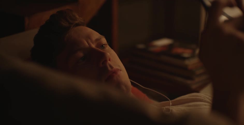 A man laying on a couch wearing earbuds and looking at a phone