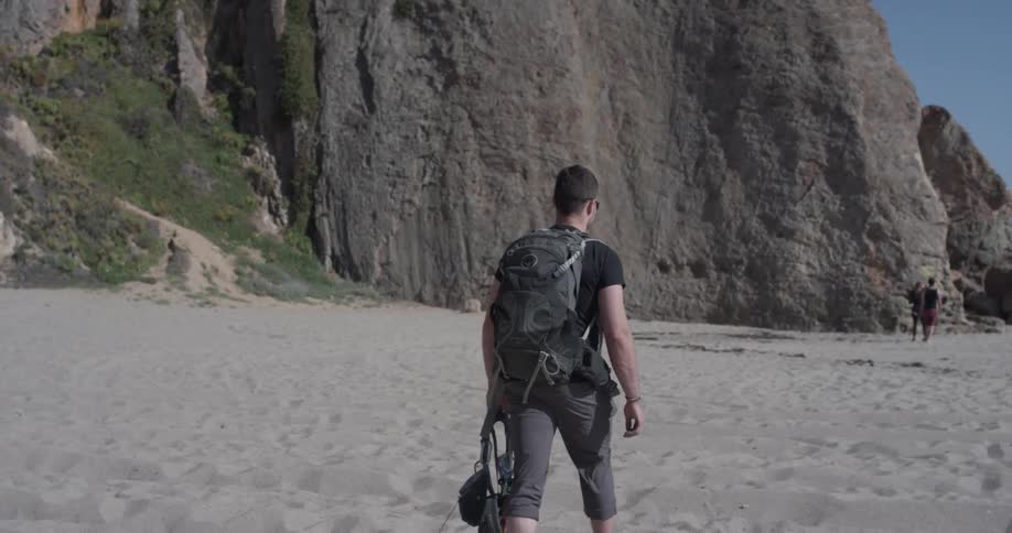 A man walking on the beach next to some cliffs