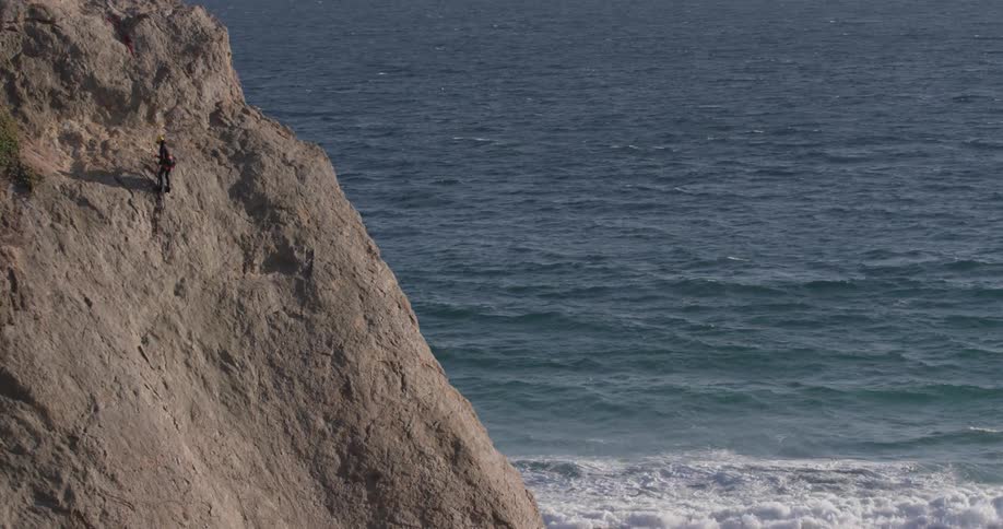 A man that is climbing up a mountain next to the ocean