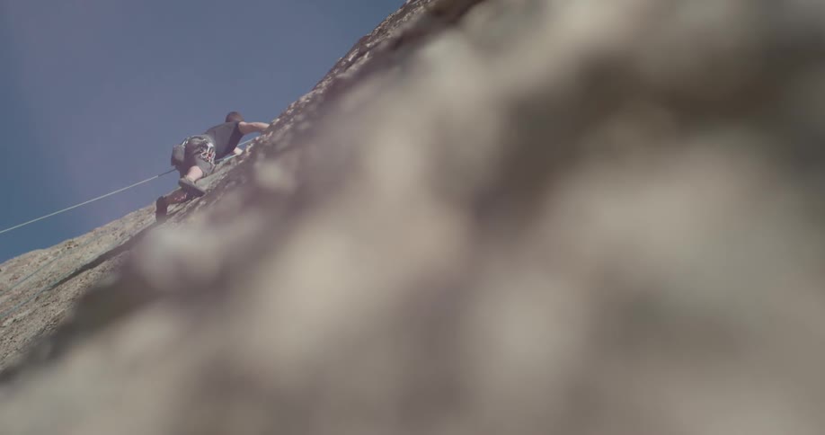 A man is climbing up a large rocky cliff