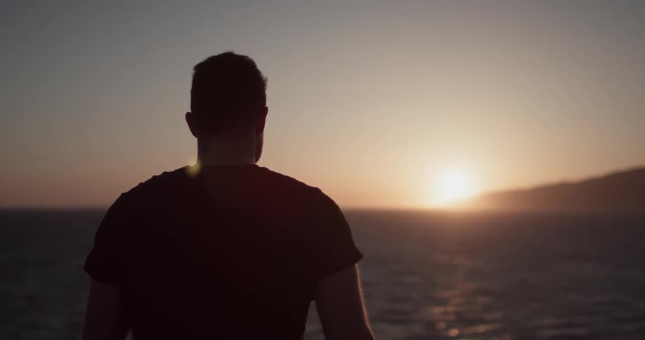 A man is looking outside at the sunset