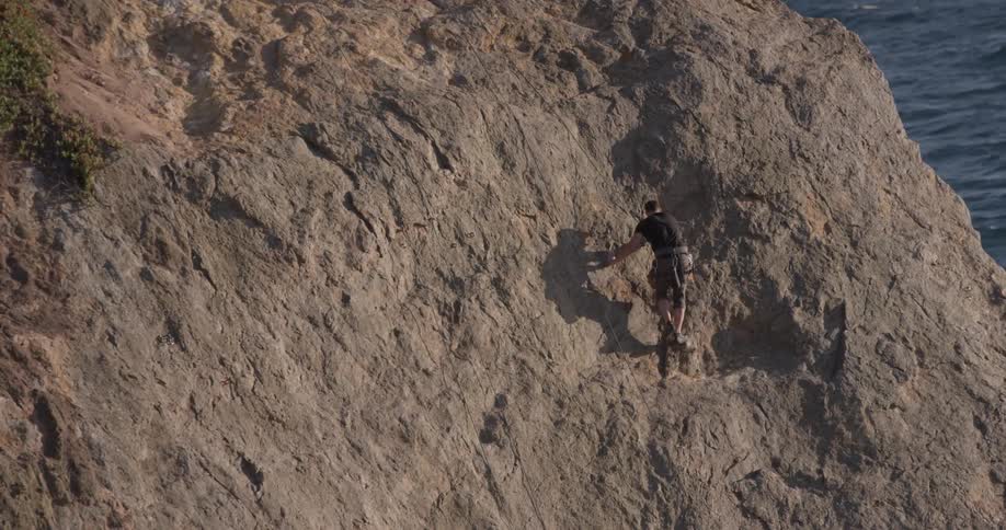 A man reaches up as he climbs a cliff