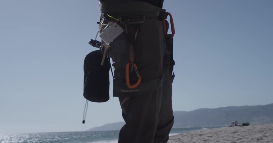 Man putting on climbing gear while standing on a beach