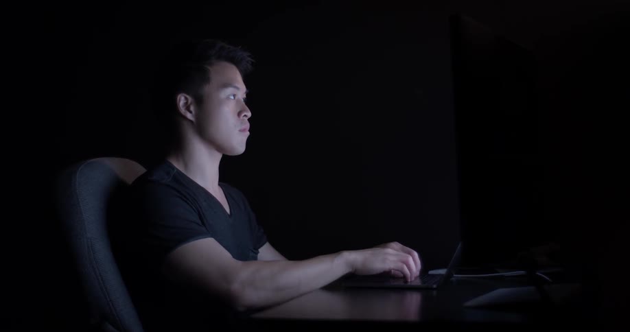 A man sitting in a dark room typing on a computer