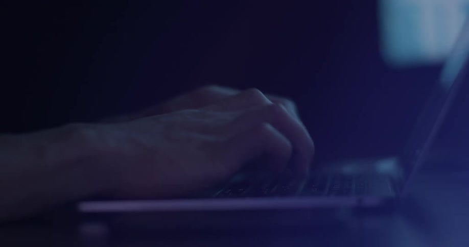 Person typing at a laptop keyboard in a dark room