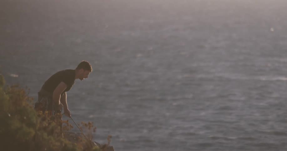 A man pulls a rope up from over the cliff