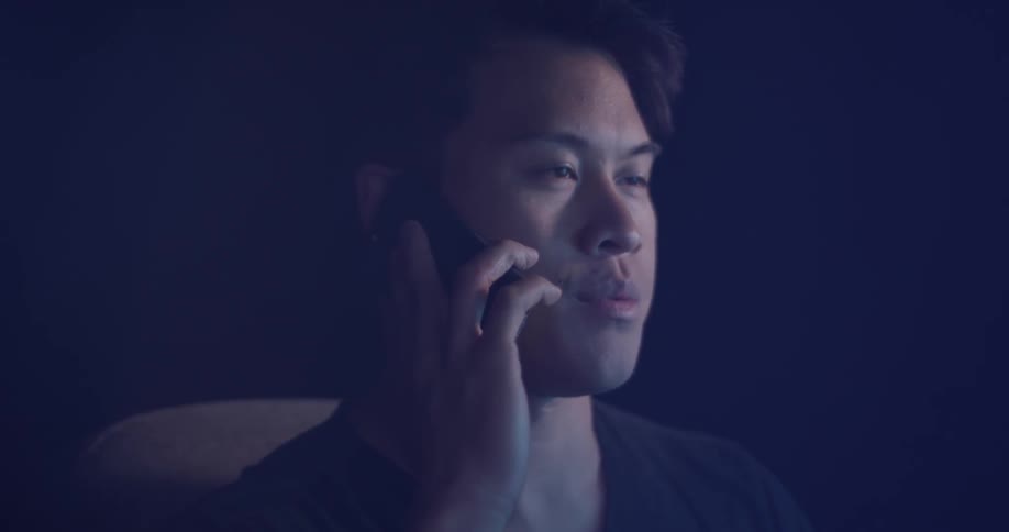 Man is sitting and talking on cell phone in dark room