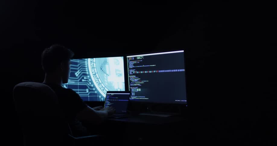 A man works at a desk on a laptop with two larger monitors