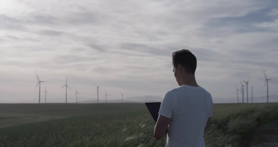 Man uses a tablet while standing in a wind farm
