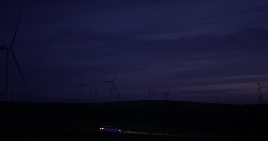 Man Driving Electric Car Through Wind Farm