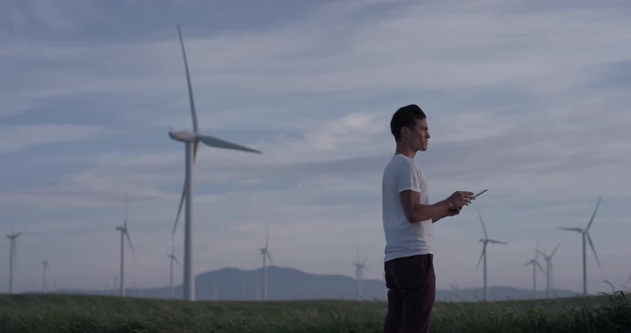 A man using a drone controller next to windmills