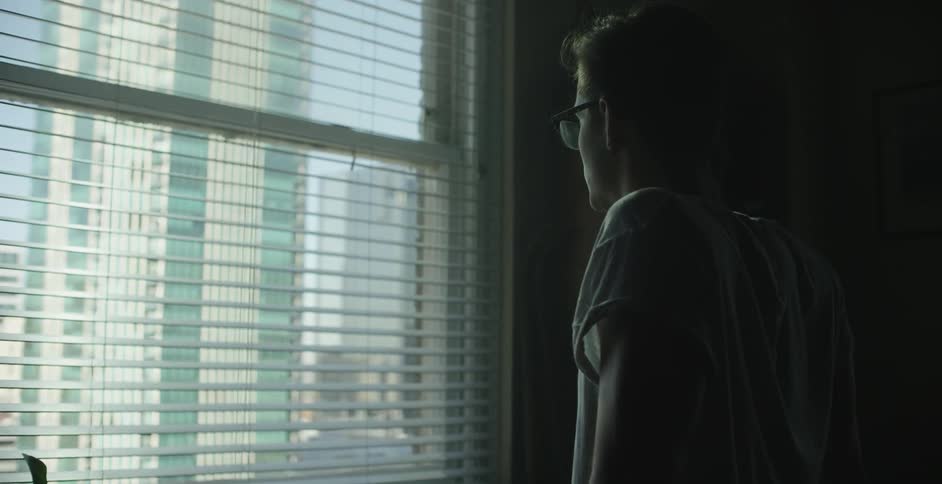 A man looking out a window that is facing a skyscraper