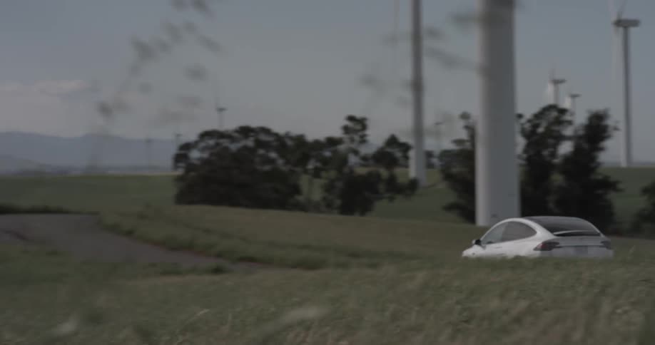 A white car driving down a road in a field near windmills