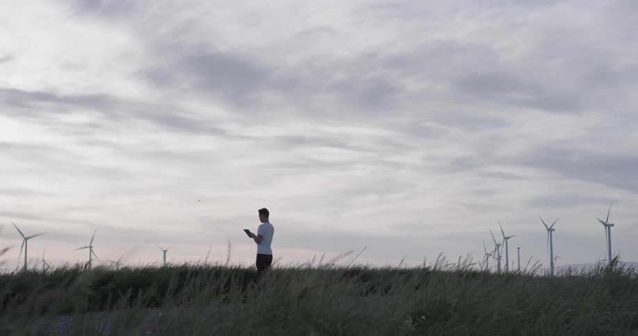 A man flying a drone in a field full of windmills