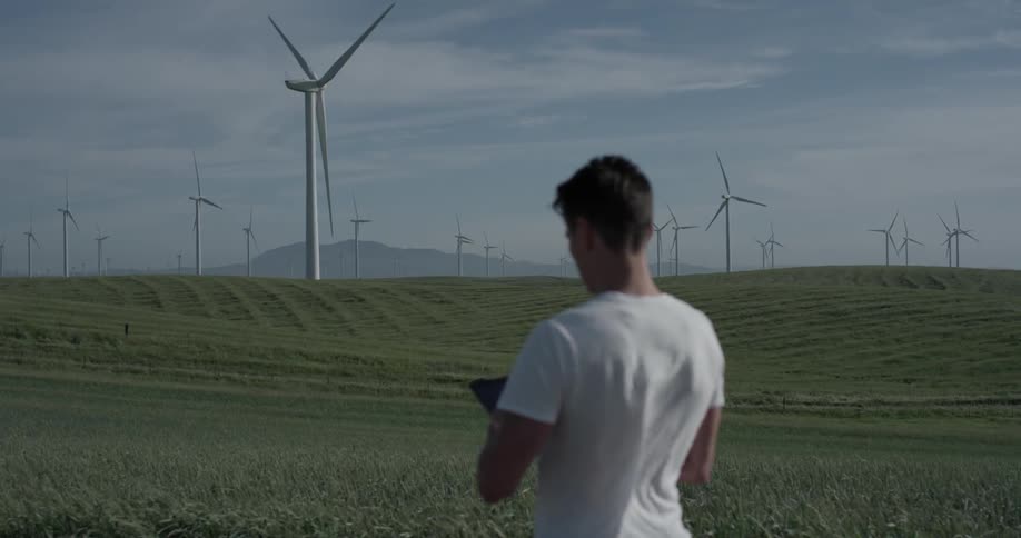 Man looks a cell phone in his hands while outdoor at windmill farm