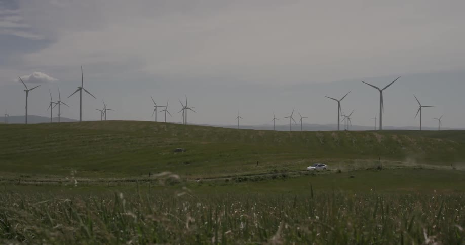 A car driving down a road passing wind turbines
