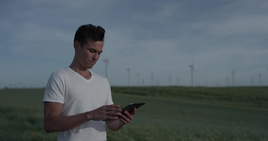 A man stands in a field surrounded by windmills and touches a tablet