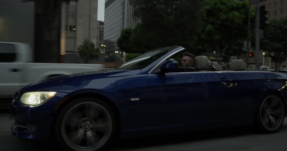 Man driving a blue convertible down a city road
