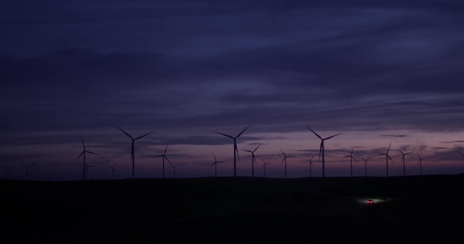 A car that is driving through a field of windmills at night