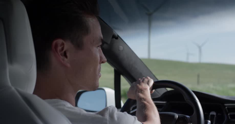 A man driving a car on a dirt road next to some grassy hills