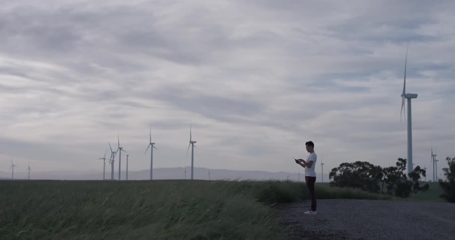 A person that is flying a drone next to some windmills
