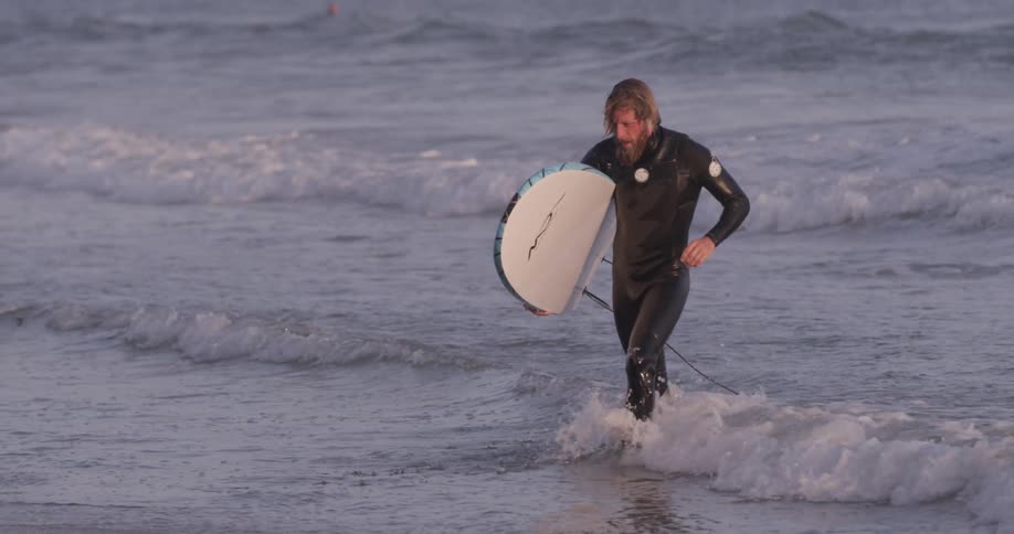 A man holding a surfboard walks from the water to the shore