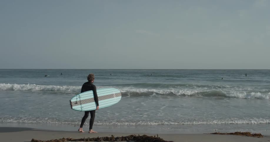 A man holding a surfboard at the edge of the coast