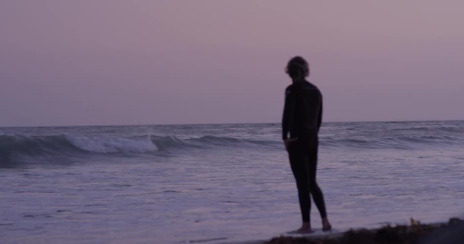 A man stands on the beach and steps into the surf at dawn