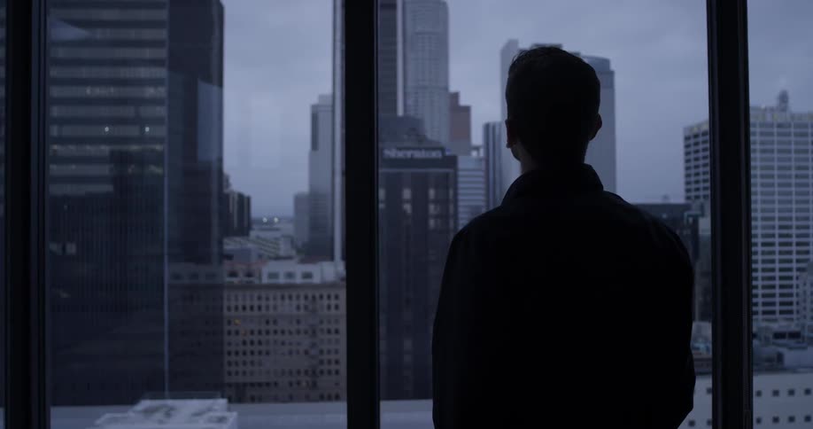 A man admires the city view from large windows