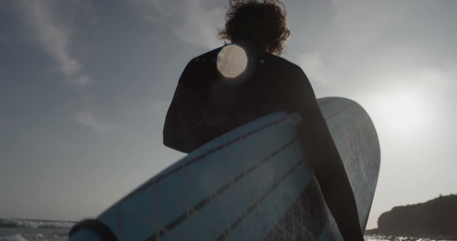 A person walking through the ocean carrying a surfboard