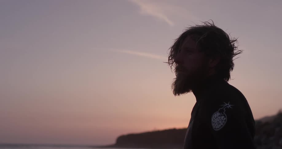 Man stands on the beach while the sun sets behind him