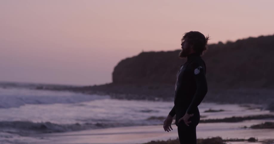 A man with his hands on his head looking at the ocean at sunset