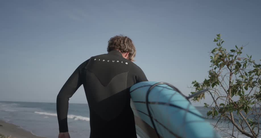 A man holding a surfboard walks toward the water