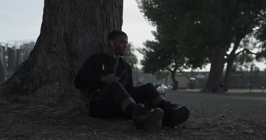 A man drinking a bottle of water at the base of a tree