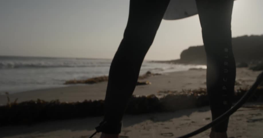Person picking up a surfboard on a beach next to the ocean