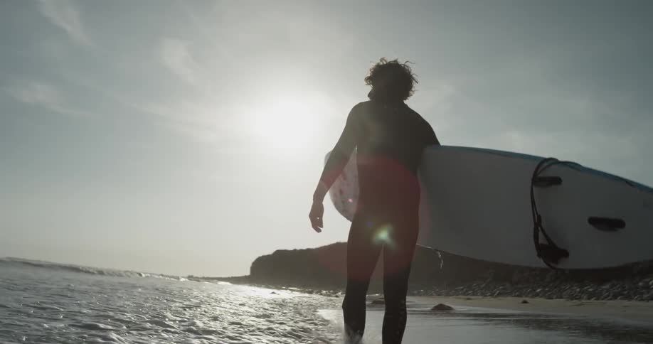 A man in a wetsuit walking along the coast carrying a surfboard
