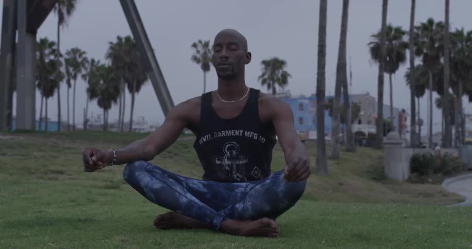 A man has his legs crossed and eyes closed sitting in the grass