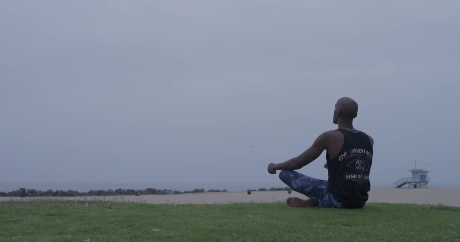Man meditates while sitting on the grass at the beach
