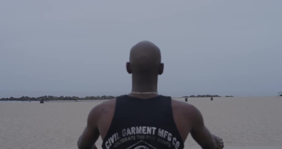 A bald man is at the beach on an overcast day