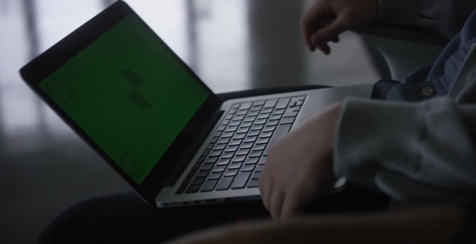 Two men sit in an open office and look at a laptop computer