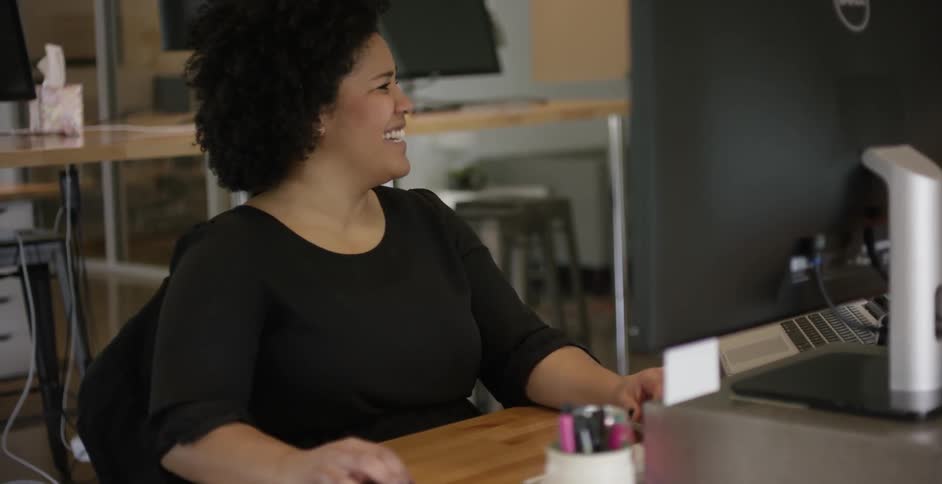 A woman at a computer workstation laughs while working