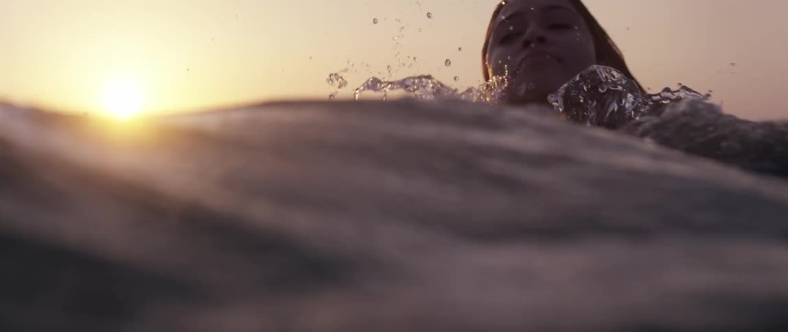 A woman with long hair swims in a large body of water at sunset