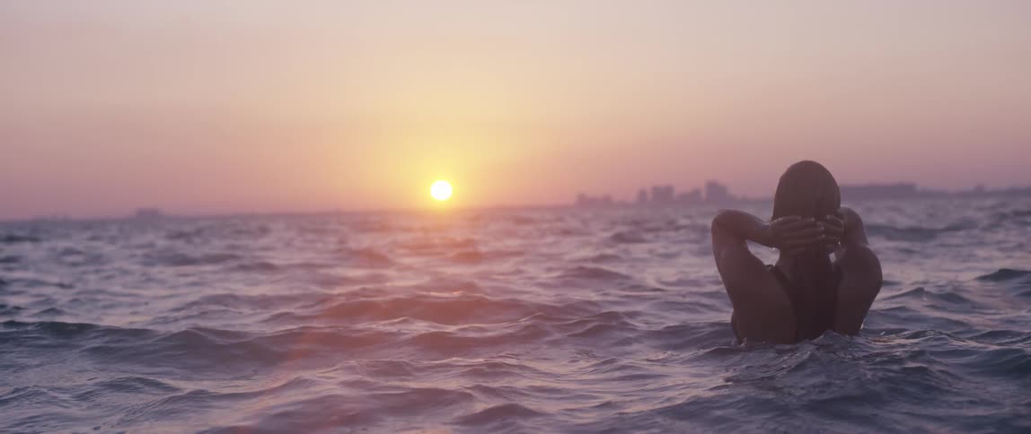 A woman swimming in the ocean at sunset