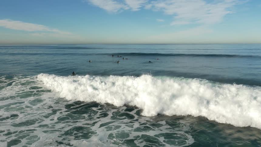 Waves crash under a partly cloudy sky
